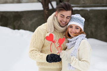 Wall Mural - Young couple in love holding red paper hearts outdoors in winter