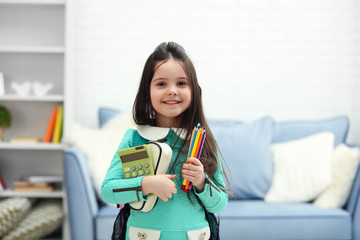 Little girl with green back pack holding stationery and calculator in living room