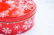 Christmas gift container.  Red, round cookie & baked goods tin container decorated in red with white snowflake print pattern, sitting in natural snow.