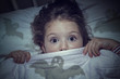 scared cute little girl under the blanket in her bed