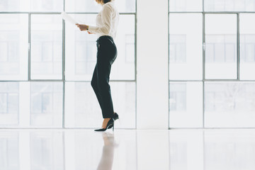 Wall Mural - Closeup photo business woman wearing suit. Open space loft office. Holding papers hands. Analyze plans, meeting, panoramic windows background. Horizontal mockup.