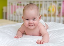 Cute And Smiling Crawling Baby Girl Lying On Belly.