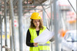 Female engineer with helmet and safety jacket on construction site examining office blueprints. Outdoors