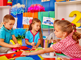 Female kid learning craft colored paper on table in kindergarten .