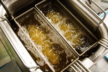 A Silver Deep Pan Industrial Kitchen Oil Fryer, With Golden Oil, Bubbling And Frying Potatoes