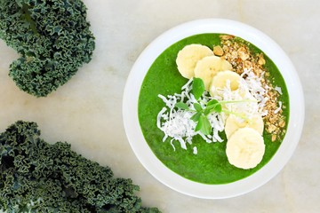 Wall Mural - Green smoothie bowl with kale, bananas, granola, and coconut. Overhead scene on white marble.