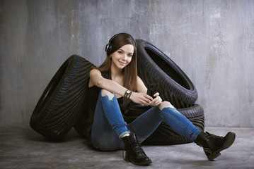 Wall Mural - young, cheerful woman with headphones sitting near the tires and