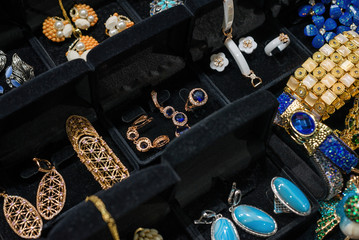 Variety of jewelry in store window. Rings with colorful gems and anamel on velvet stands for sale.