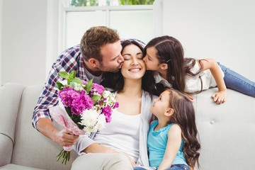 father and daughter kissing mother sitting on sofa