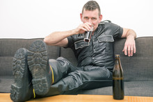 Man In Fetish Leather Gear Sitting On Couch