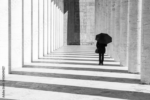 Fotografia Donna con ombrello in un corridoio porticato in bianco e nero