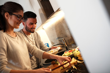 Young couple in kitchen preparing together  vegetarian meal.Preparing fruit salad.Evening.