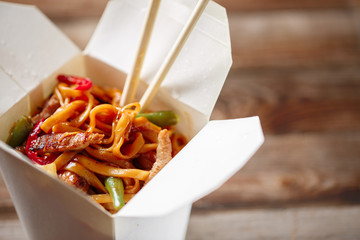 Noodles with pork and vegetables in take-out box on wooden table