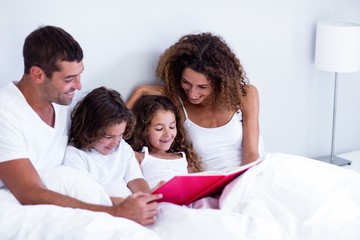 Wall Mural - Family reading book together on bed