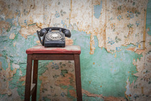 Old Vintage Phone On A Chair Stool In Front Of Grunge Wallpaper Background