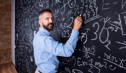 Hipster teacher writing on big blackboard with mathematical symb