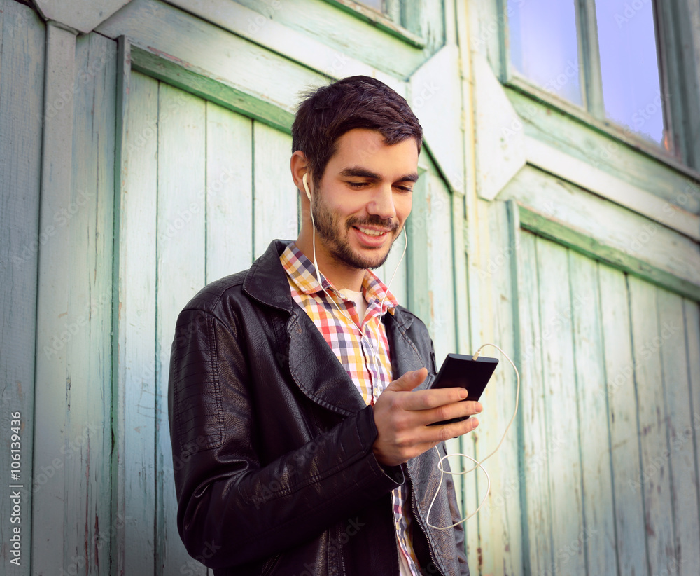 Young man listening to music on a house wall background