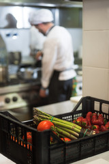 box of vegetables in the kitchen with the chef cooking in the background