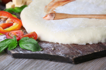 Canvas Print - Fresh dough prepared for pizza with tomatoes and sliced pepper on a wooden board, close up