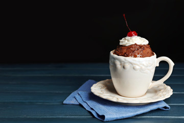 Wall Mural - Chocolate mug cake with cream and cherry on a table in front of dark background