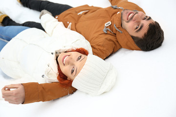 Poster - Young couple lying on the snow outdoors in winter