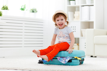 Wall Mural - happy child girl packs clothes into suitcase for travel, vacatio