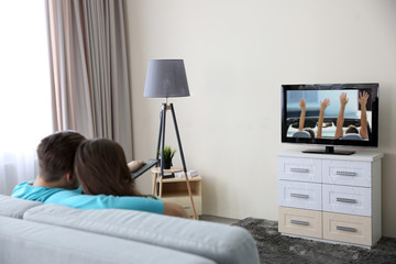 Wall Mural - Young couple watching TV on a sofa at home