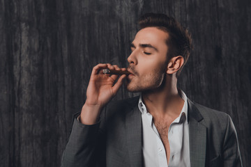 Wall Mural - Handome brutal man in suit on the gray background smoking a ciga