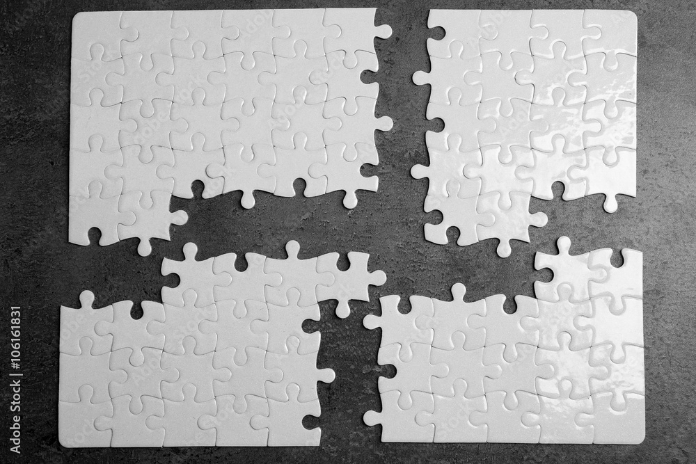 Four parts of white jigsaw puzzle with missing pieces on grey background