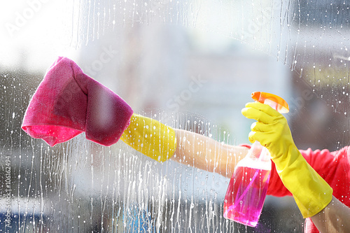 Fotografie, Obraz Woman in a rubber glove cleaning window with sponge and detergent, close up