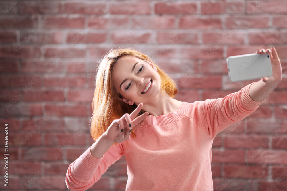 Young attractive girl taking selfie with mobile phone on brick wall background