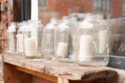 White Big Candles In Glass Jars On A Retro Wooden Table Outdoors