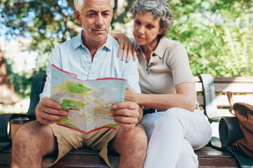 Wall Mural - Senior tourist sitting on a park bench with a city map