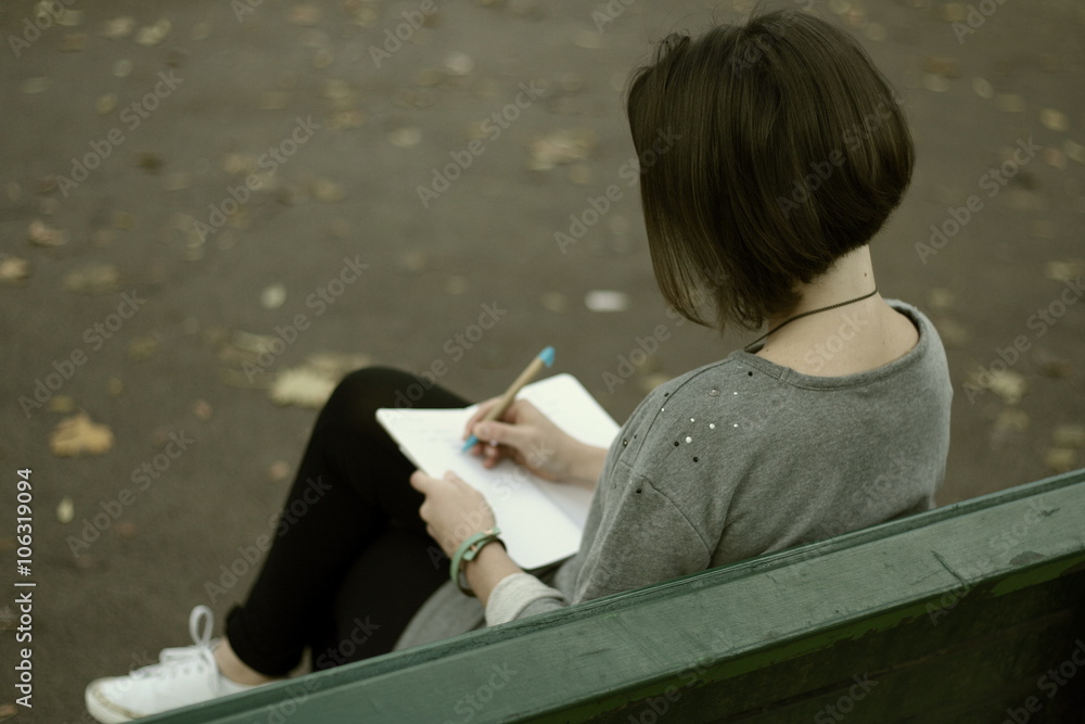 Brunette girl siting on the park bench and writing notes into her ...