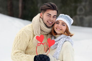 Wall Mural - Young couple in love holding red paper hearts outdoors in winter