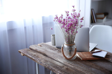 Modern interior. Comfortable workplace. Wooden table with beautiful bouquet of flowers and laptop on it, close up