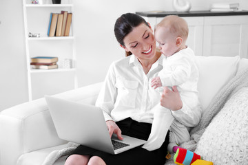 Wall Mural - Businesswoman with baby boy on couch working from home using laptop