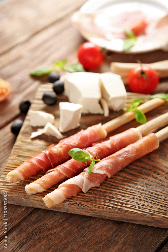 Bread sticks grissini with prosciutto ham on a  wooden board, close up