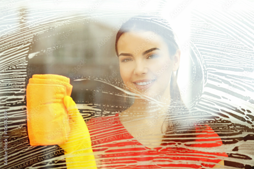 Young woman washing window glass with duster inside