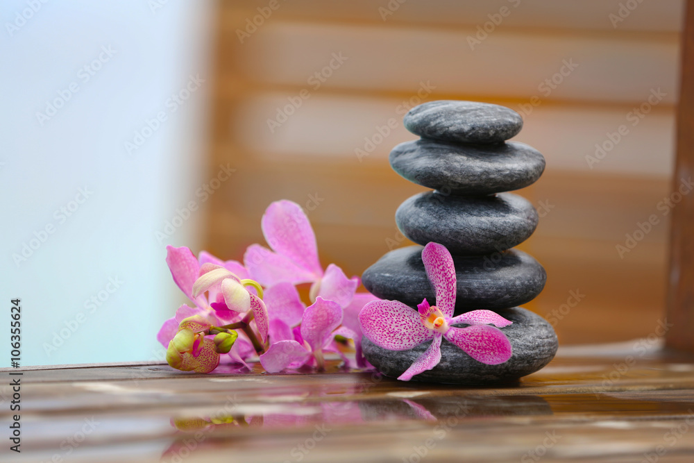 Stack of spa stones with pink orchids on wooden wet bridge