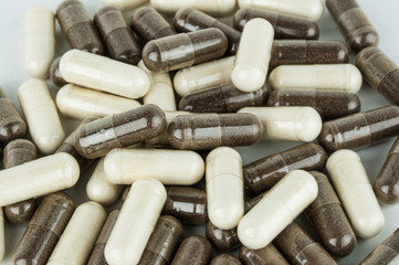 Pile of brown herbal and white capsules