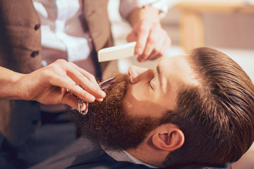 Professional barber cutting beard of handsome man