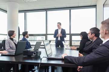 Wall Mural - Successful team leader and business owner  leading in-house business meeting, explaining business plans to his employees. Business and entrepreneurship concept.