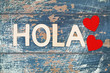 Hola (Hello in Spanish) written with wooden letters on rustic surface and two red hearts
