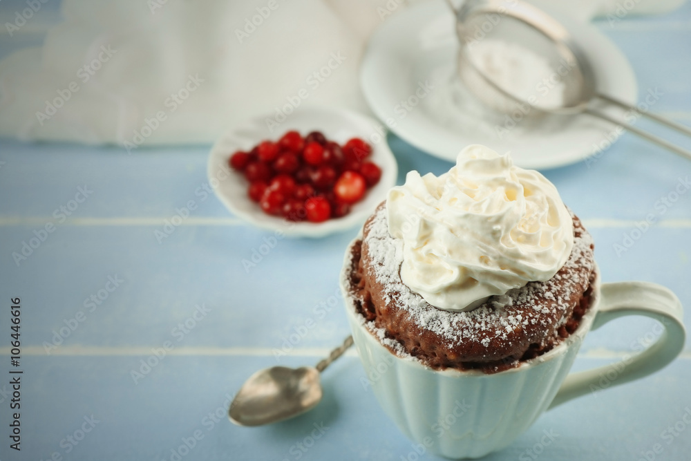 Mug cake with cream and cranberry on blue wooden background
