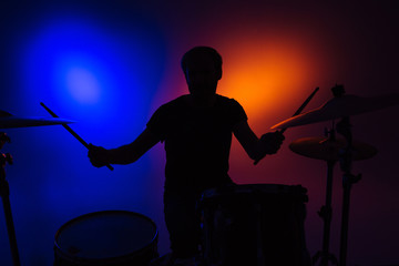 Silhouette of man drummer sitting and playing drums with sticks