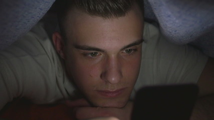 Attractive young man using a smart phone in bed