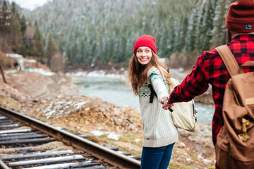 Wall Mural - Happy young couple holding hands and walking along railway