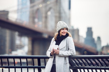 Happy Smiling Adult Tourist Woman Holding Paper Coffee Cup And Enjoying The New York City View And Brooklyn Bridge