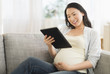 © JGI/Tom Grill/Blend Images - Pregnant Japanese woman using digital tablet on sofa